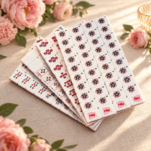 Stacked sheets of white American Mahjong tiles showing rows of navy stars, red-and-blue circles and red floral motifs.