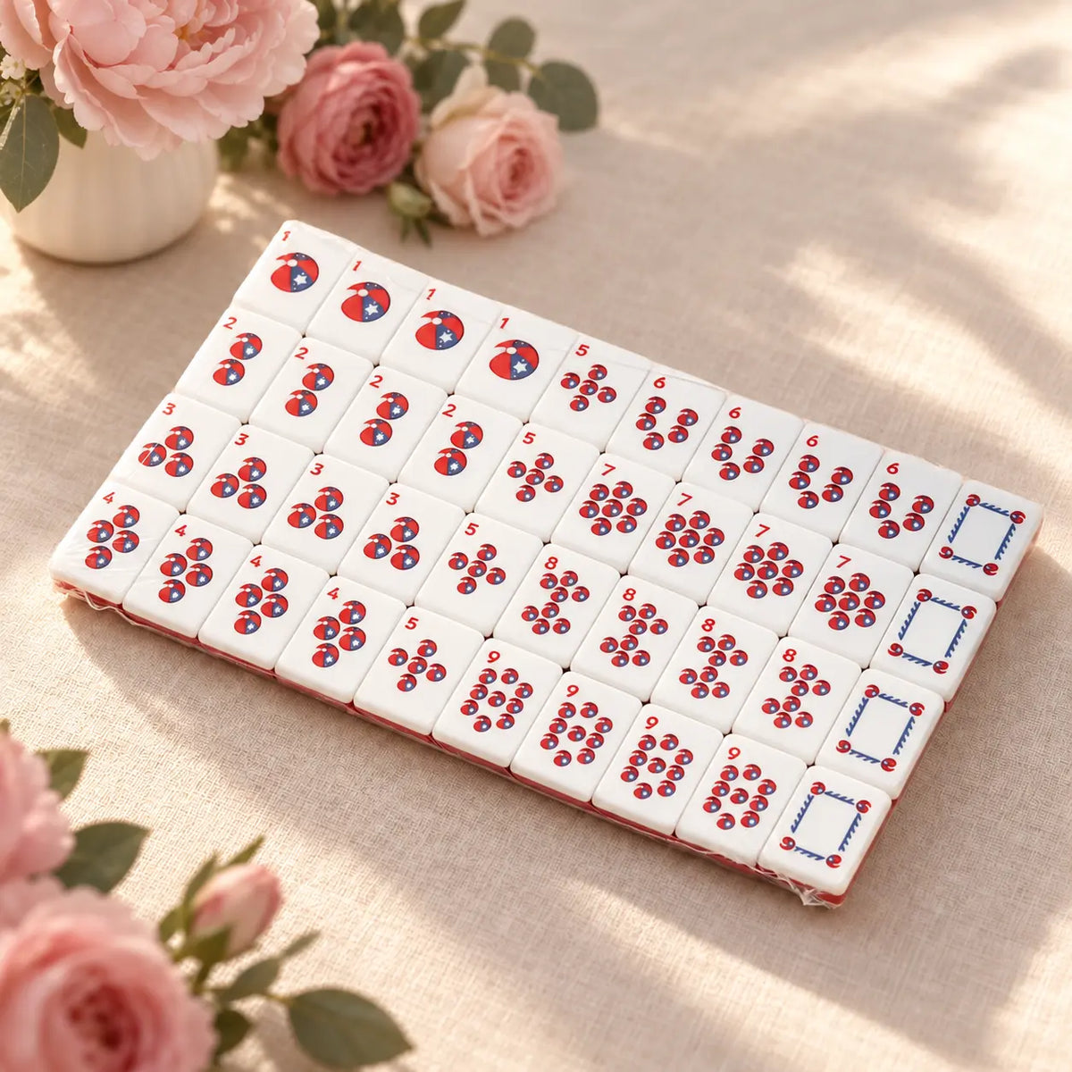 White Mahjong tiles arranged in rows of red-and-blue circle patterns and outlined rectangular faces beside pink roses.