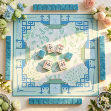 Pale blue Mahjong mat with green floral motifs and geometric corners, surrounded by four rows of blue-backed tiles.