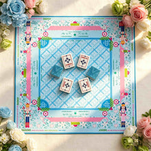 Blue crosshatch Mahjong mat with a pink floral border and illustrated figures, displaying four wind tiles in the center.